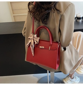 Détail du sac rouge structuré avec fermoir doré rotatif et élégant foulard en soie imprimé