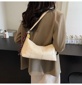 Detail of cream leather shoulder bag with decorative plaid scarf and smile charm pendant