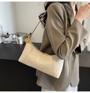 Minimalist beige hobo bag with yellow smiley face pendant shown on female model