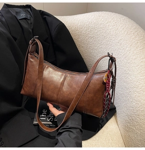 Close-up of a vintage brown leather shoulder bag with fine stitching and a woven cord charm