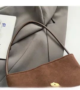 Detail eines bequemen Schultergurts und Goldlogo auf brauner Wildleder-Beuteltasche