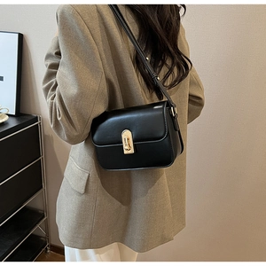 Close-up of a black leather crossbody bag with a gold metal lock shown on a model