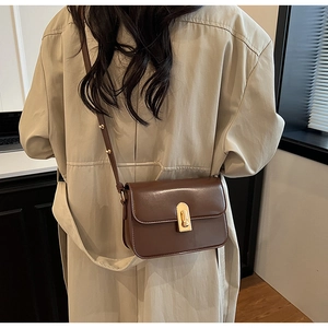 Detail view of a vintage brown crossbody bag with a gold metal clasp worn by a model