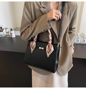 Détail du sac à main noir en cuir avec fermoir doré et foulard en soie sur la poignée