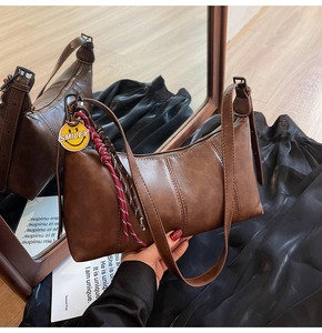 Brown vintage underarm bag with smiley pendant and woven rope detail in close-up view