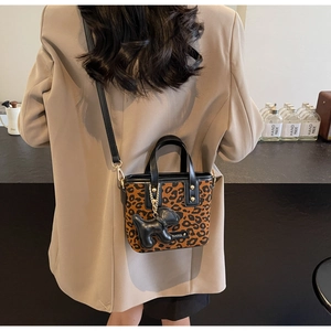 Détail du sac seau léopard avec breloque chiot noir et plaque logo en métal de luxe