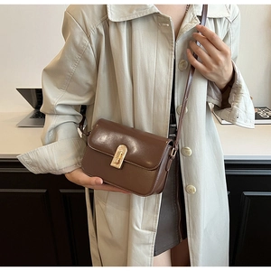 Detail of a brown leather crossbody bag with a golden metallic clasp on an office desk