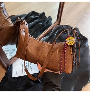 Detailed close-up of brown retro shoulder bag with smiley charm and woven strap detail
