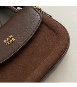 Detail of dark brown leather handbag featuring gold PAN TOR logo and suede texture contrast