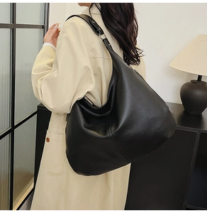 Detail einer großen schwarzen Hobo-Tasche aus Leder mit verstellbarem Gurt, getragen von Model