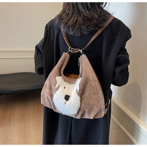 Brown corduroy backpack with plush 3D dog detail shown on a model in an indoor setting