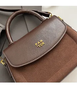 Detail of dark brown handbag showing leather splicing, gold logo, and premium metal hardware