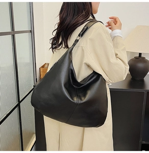 Detail der schwarzen Ledertasche mit breitem Gurt auf einem beigen Trenchcoat