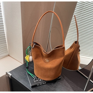 Detail einer dunkelbraunen Wildleder-Eimertasche mit Goldlogo und buntem Anhänger auf Büchern
