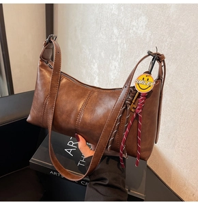 Detail of vintage brown leather shoulder bag with yellow smiley face charm and woven rope decoration