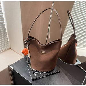 Detailansicht der braunen Wildleder-Beuteltasche mit Goldlogo und orangefarbenem Anhänger