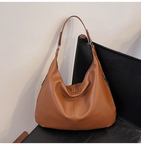 Detailansicht der großen braunen Hobo-Tasche mit Litchi-Textur auf einem schwarzen Stuhl