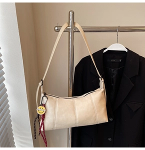 Detail of beige underarm bag with vertical stitching and a yellow smiley face charm