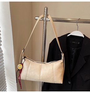 Detail of a cream underarm bag featuring vertical stitching and a smiley face charm