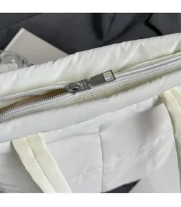 Detail view of smooth silver metal zipper on white quilted puffer tote shoulder bag