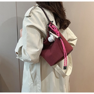 Detail der weinroten Beuteltasche mit rosa Anhänger an einem beigen Trenchcoat getragen