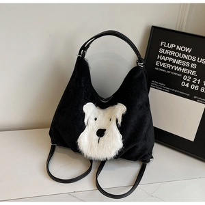 Detail of black corduroy tote with a white plush dog patch and slim leather straps