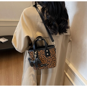 Détail d'un sac léopard avec breloque chien en cuir noir et plaque dorée de logo