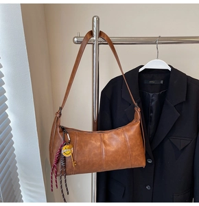 Detail of vintage brown shoulder bag with yellow smiley charm on a minimalist coat rack