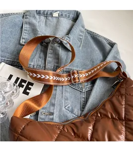 Detail of a brown quilted puffer bag featuring a glossy finish and patterned wide strap