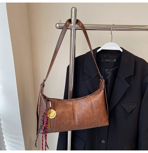 Detailed view of brown retro shoulder bag with vertical stitching and smiley face charm