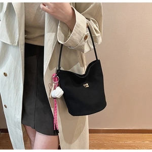 Detail der schwarzen matten Beuteltasche mit goldenem Logo und rosa gewebtem Anhänger