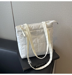 Detail of white quilted tote bag with square stitching and top zipper on a desk