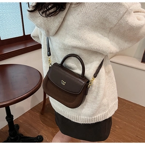 Brown leather handbag detail featuring a gold metallic logo and sleek curved top handle
