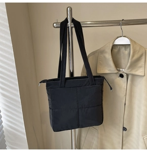 Detail of black quilted shoulder bag featuring glossy water-resistant fabric and zippers