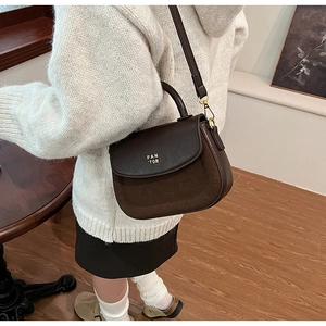 Close-up of dark brown paneled crossbody bag with golden logo and textured leather