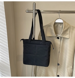 Detail of black quilted shoulder bag with puffy texture and metal zipper puller