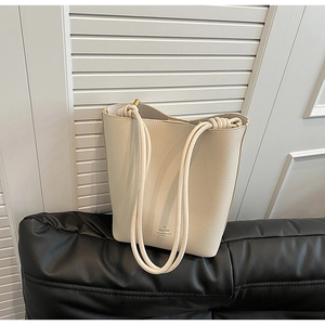 Close-up of cream leather bucket bag with litchi texture and braided rope straps