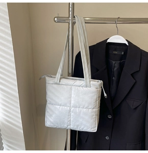 Detail of light gray quilted puffer tote bag with metallic finish and top zipper closure