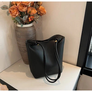 Detail of black pebbled leather bucket bag featuring a unique knotted shoulder strap accent