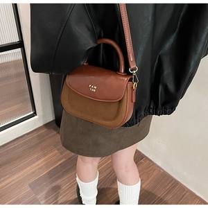 Close-up of brown patchwork leather saddle bag with gold logo and handle detail