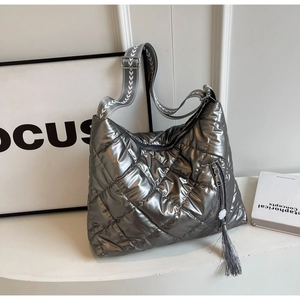 Detail of silver quilted puffer bag featuring wide woven strap and tassel accent