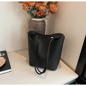 Detail of black pebbled leather bucket bag with gold hardware and thin shoulder straps