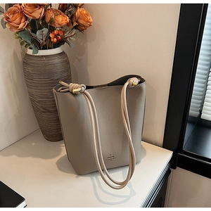 Close-up of beige litchi pattern bucket bag with knot shoulder strap and metal details