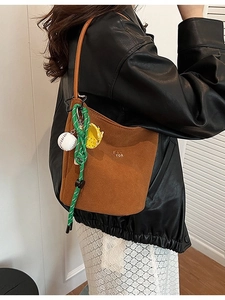 Braune matte Eimer-Tasche aus Wildleder mit sportlichen Anhängern an einem schicken Model