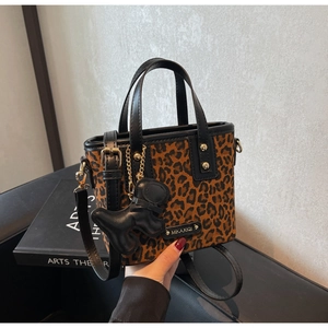 Détail d'un sac seau léopard avec charme de chien en cuir noir et finitions dorées