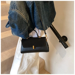 Detail of a black crossbody bag with matte flap and golden metal clasp on a textured background