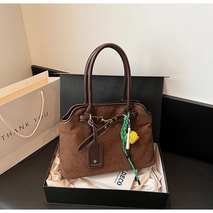 Detail of vintage brown suede tote bag with decorative green woven charm in a gift box