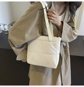Detailed view of a white quilted puffer shoulder bag on a beige trench coat