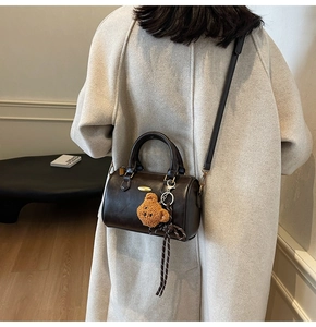 Detail of dark brown Boston bag with golden hardware and cute teddy bear charm