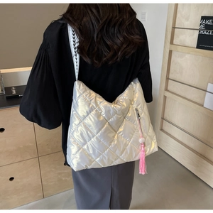 Detail of silver quilted shoulder bag featuring pink tassel and geometric woven strap